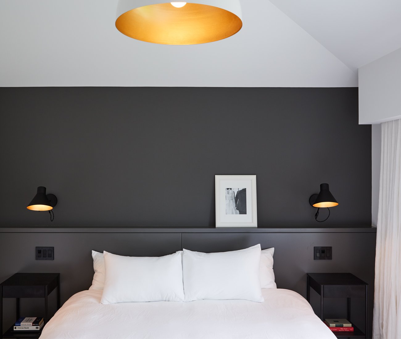 Master bedroom featuring his-and-hers nightstands illuminated by gold-accented black sconces from Luminaire Authentik.
