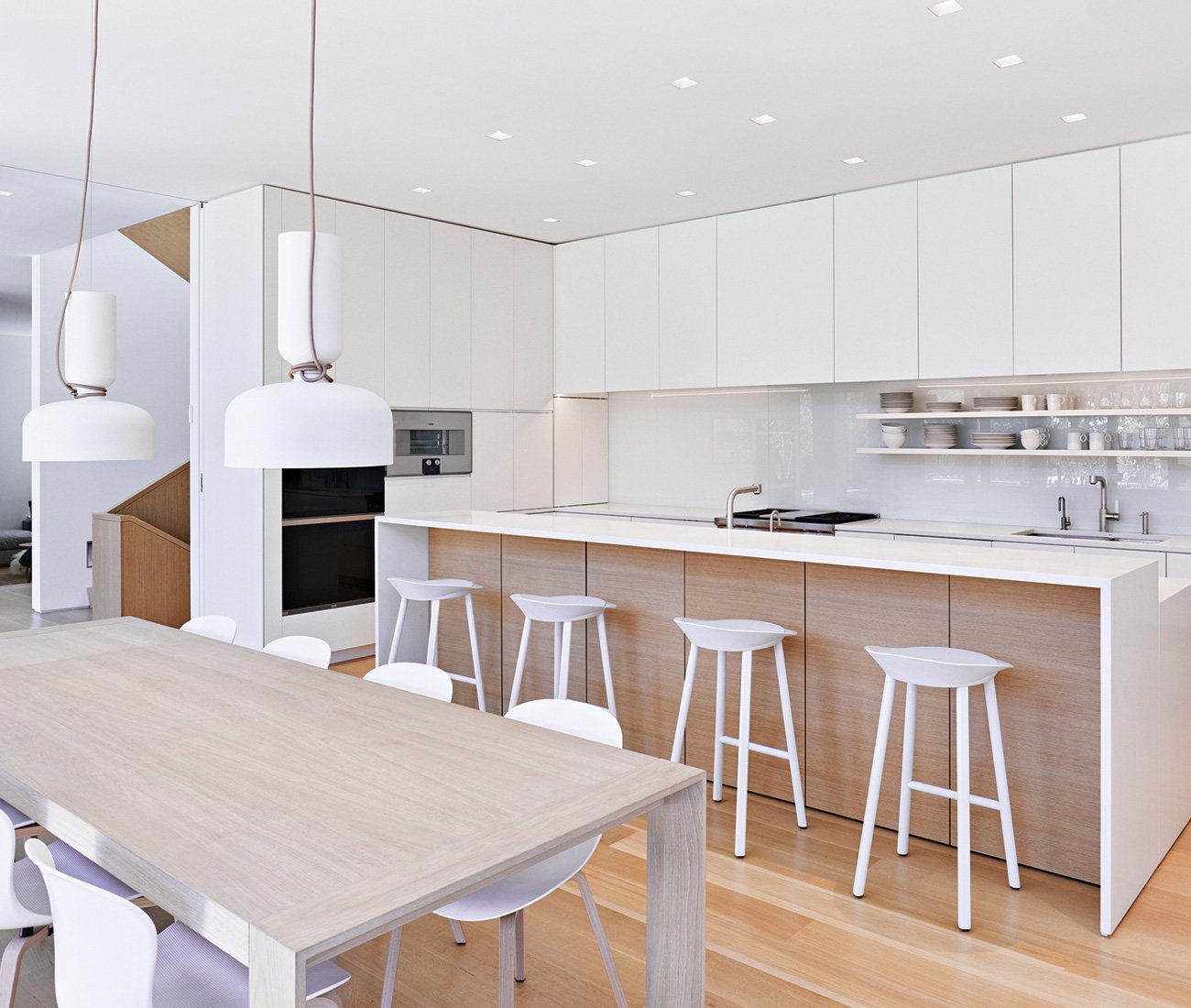 AKB ATELIER KASTELIC BUFFEY Minimalist Home Toronto Modern dual-tone kitchen featuring white and wood laminate cabinets extending to the ceiling, a long island, a dining table, and stylish light pendants.
