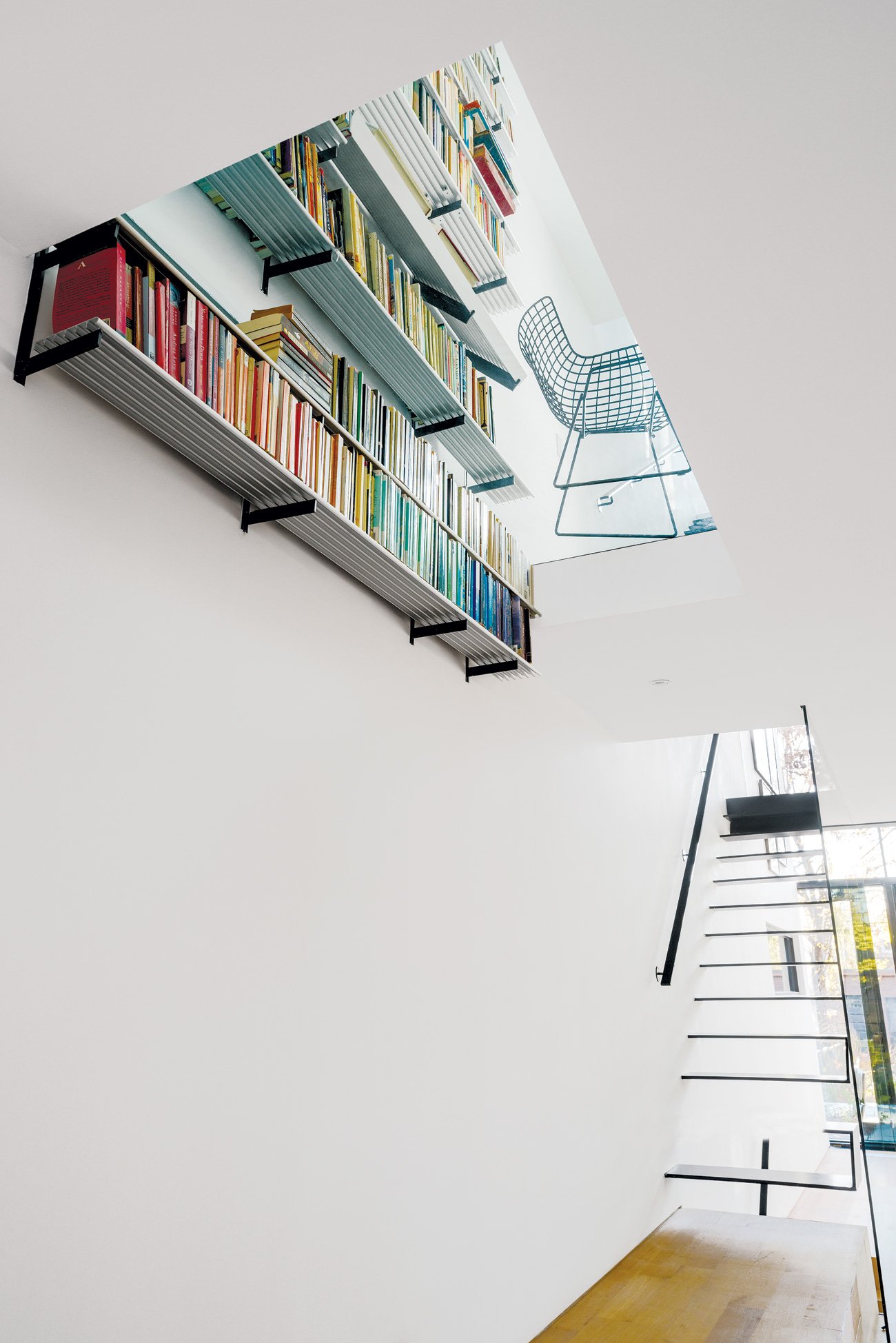 Designer Johnson Chou aluminum bookshelves on the first floor appear to burst through the glass floor of the second of this modern east end home