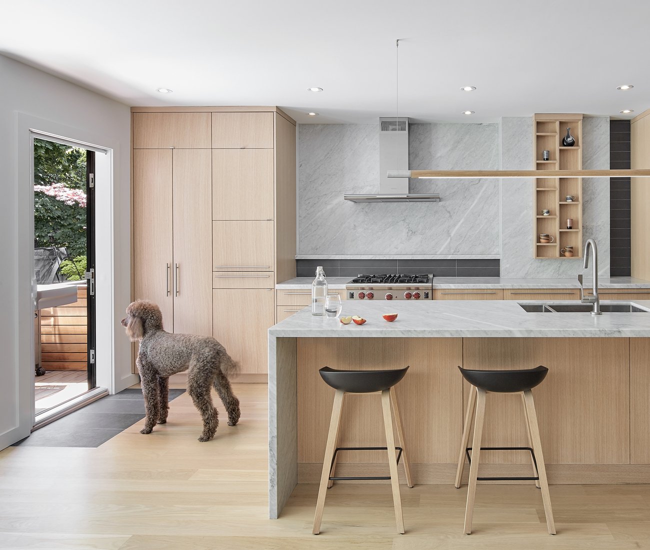 Wood finished kitchen with a poodle looking outside the sliding door
