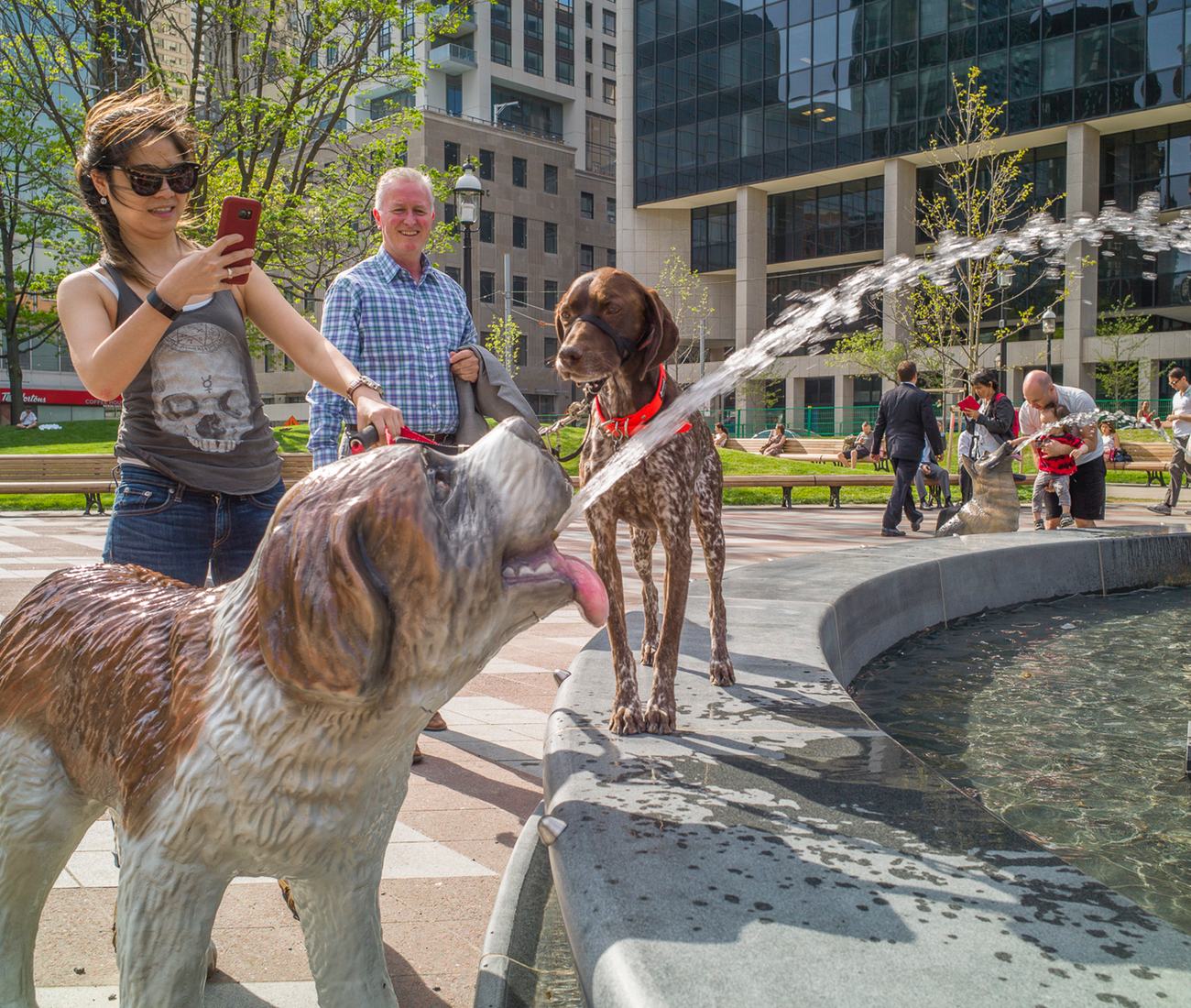 A young woman take a picture of her dog at pet friendly Berczy Park in Toronto